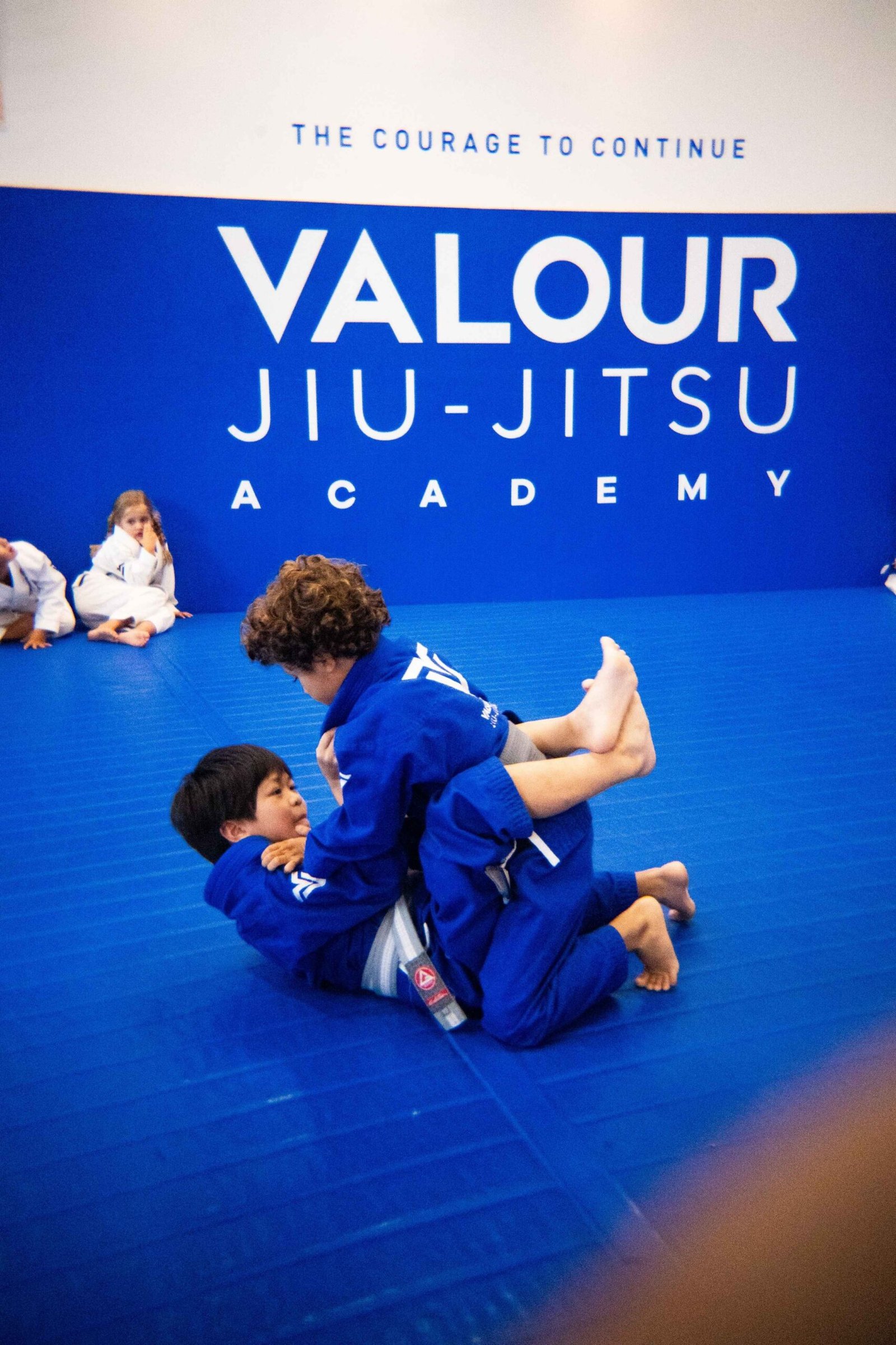 Two children in blue gis practising Brazilian Jiu-Jitsu on the mat at Valour Jiu-Jitsu Academy in Fulham, London